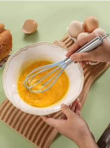 Macro detail of hand using a blue silicone whisk with stainless steel handle in a white bowl