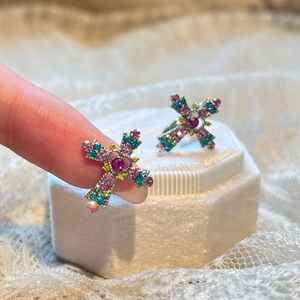 Cross-shaped earrings with colorful pavé rhinestones on a white velvet jewelry box
