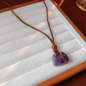 Macro detail of purple stone pendant with wooden bead on brown leather necklace