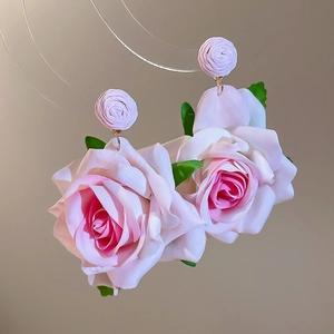 Detailed view of handmade pink silk fabric rose earrings with green leaves and hooks