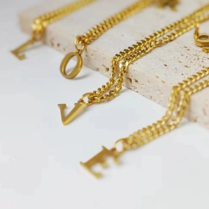 Collares de letras doradas en acero con cadena cubana gruesa formando LOVE en travertino