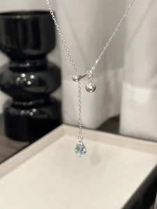 Macro shot of silver teardrop necklace with blue sapphire and polished metal detail