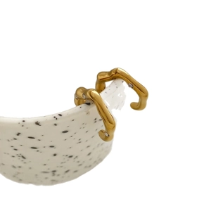 Gold plated stainless steel wavy earrings with diamond inlay shown on ceramic edge