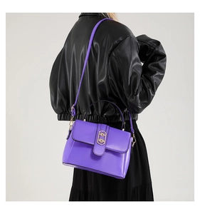 Detail of purple crossbody bag with gold oval buckle worn by model in black jacket