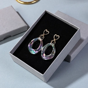 Elegant gold heart earrings with iridescent oval pendants displayed in a gray jewelry box