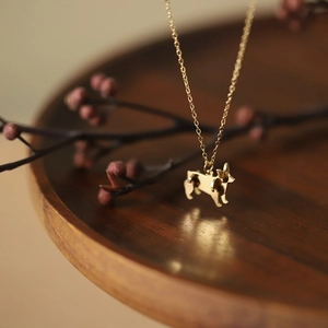 Detailed close-up of golden corgi dog pendant necklace on a premium wood and berry background