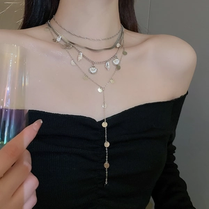 Detail of layered silver chain necklace with shell charms and metallic sequins on neck