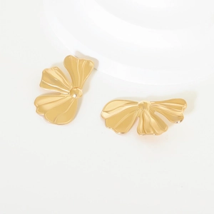 Detail shot of golden metal flower earrings with bow design on a minimalist white platform