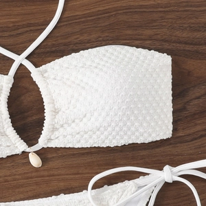Detail of white crinkle fabric bikini top with natural shell pendant on wood texture