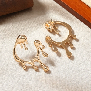 Macro shot of gold molten metal earrings with fluid texture on beige fabric background