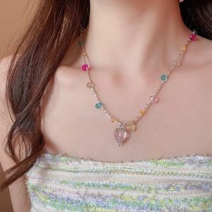 Dettaglio di una collana di perline con un ciondolo a fragola in vetro rosa sul collo