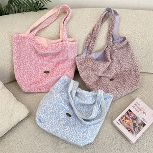 Détail des sacs cabas en peluche à motif léopard en rose, violet et bleu sur un canapé