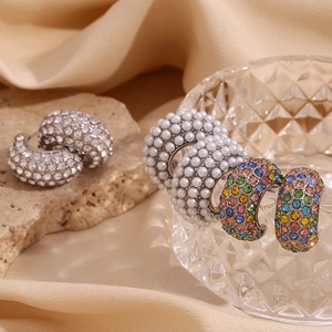 Detailed view of C-shaped earrings with pearls and colorful crystals on beige silk