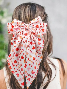 Detail of a large white bow hair clip with red hearts and LOVE prints for Valentine's Day
