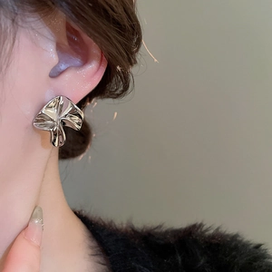 Close-up of irregular pleated flower earrings in silver on model showing artistic texture