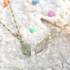 Macro view of conch shell pendant necklaces with colorful enamel beads on a sandy beach