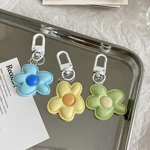Three colorful plush flower keychains in blue, yellow, and green on a silver tray