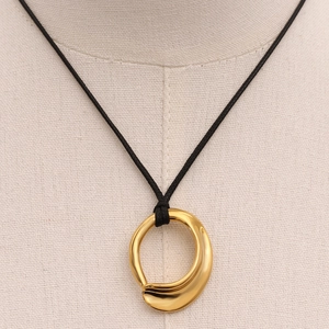 Minimalist gold irregular pendant necklace on black cord displayed on a beige mannequin