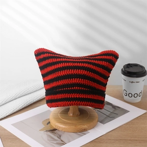 Detail of red and black striped knitted beanie with cute cat ears on wooden stand