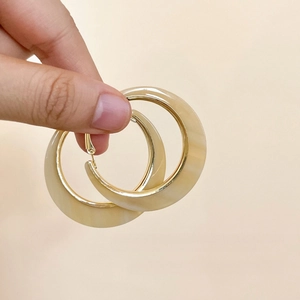 Macro detail of beige marble texture acrylic hoop earring with gold metal accents