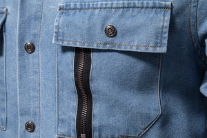 Macro shot of light blue denim shirt showing twill texture, gold stitching and metal zipper
