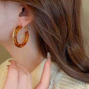 Close-up of tortoise shell resin hoop earrings with gold metal trim worn by a model
