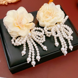 Close-up of cream floral earrings with white pearl tassels on a black jewelry box