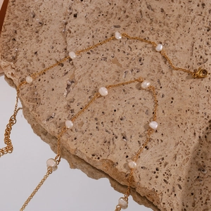 Detailed macro view of a gold chain necklace with white freshwater pearls and lobster clasp