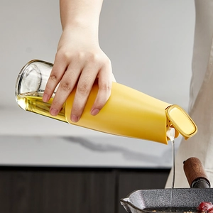 Automatic gravity glass oil dispenser bottle with yellow lid pouring oil in kitchen