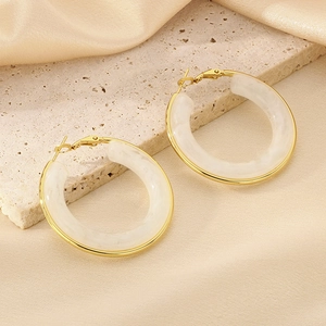 Close-up of milky white resin hoop earrings with gold-plated metal borders on silk