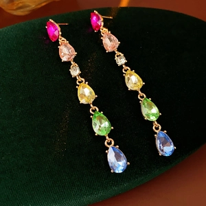 Detailed view of rainbow teardrop crystal earrings with gold chains on green velvet
