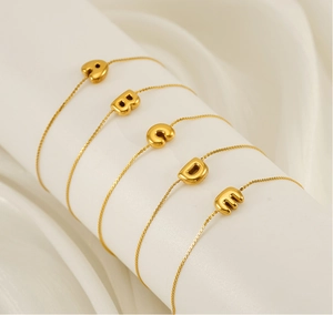 Close-up of gold chain bracelets with 3D letter charms on a white pedestal