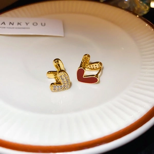 Détail de boucles d'oreilles cœur en or avec émail rouge et zircon blanc sur plat blanc