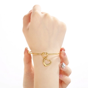 Detail of 18K gold plated knotted bangle with hollow heart charm on model wrist