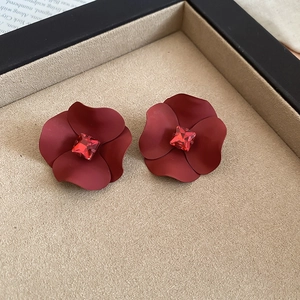 Detail of matte burgundy flower stud earrings with a red crystal center on a beige tray