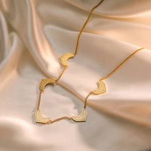Minimalist gold-plated titanium necklace with five textured heart pendants on silk fabric