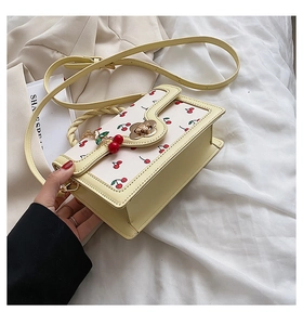 Detail of yellow cherry print bag with floral gold clasp and woven handle on fabric