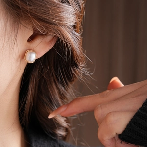 Detail view of a square pearl earring with gold frame worn by a model in soft lighting