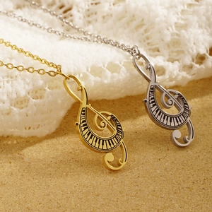 Gold and silver treble clef pendant necklaces with piano key details on lace background