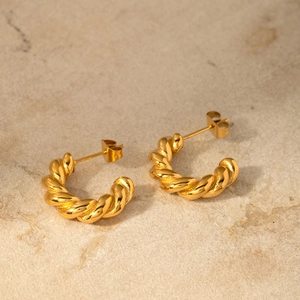 Close-up of twisted 18K gold-plated C-shaped hoop earrings on a textured stone surface