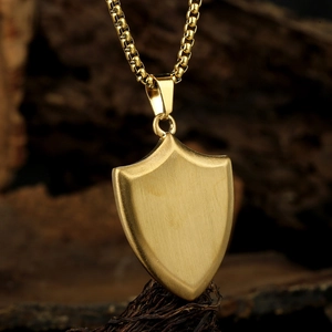 Brushed gold shield pendant necklace with box chain on a vintage wooden surface