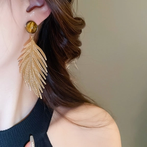 Close-up of golden feather earring with tiger eye stone worn on a model's ear