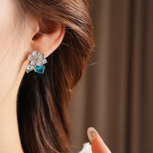 Macro detail of silver needle flower earring with blue cubic zirconia on model ear