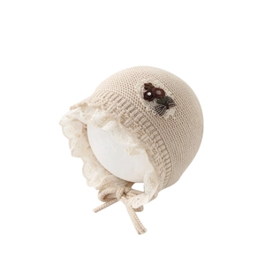 Beige knitted baby princess hat with white lace trim and floral bow detail