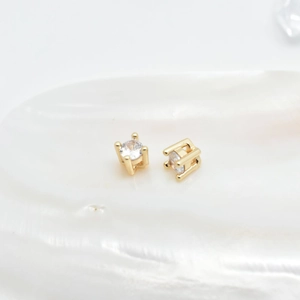Gold prong-set round cubic zirconia stud earrings displayed on a white shell