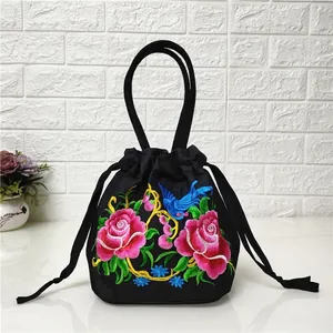 Detail of floral embroidery with blue bird and pink roses on black canvas bucket bag