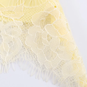 Macro view of light yellow lace fabric featuring exquisite floral embroidery and fringe