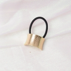 Detail of minimalist black hair tie with textured gold metal buckle on silk fabric