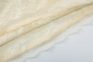 Close-up of cream white lace fabric showing intricate floral hollow patterns and stitching