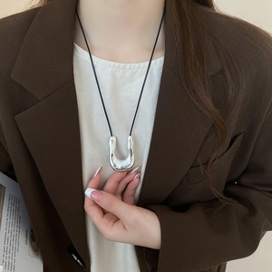Macro detail of a silver horseshoe pendant necklace with a black cord on a chic model